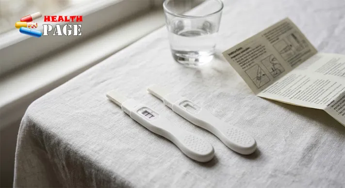 Two home pregnancy test sticks on a light surface, one showing a positive result and one showing a negative result, beside a glass of water and an instruction leaflet.